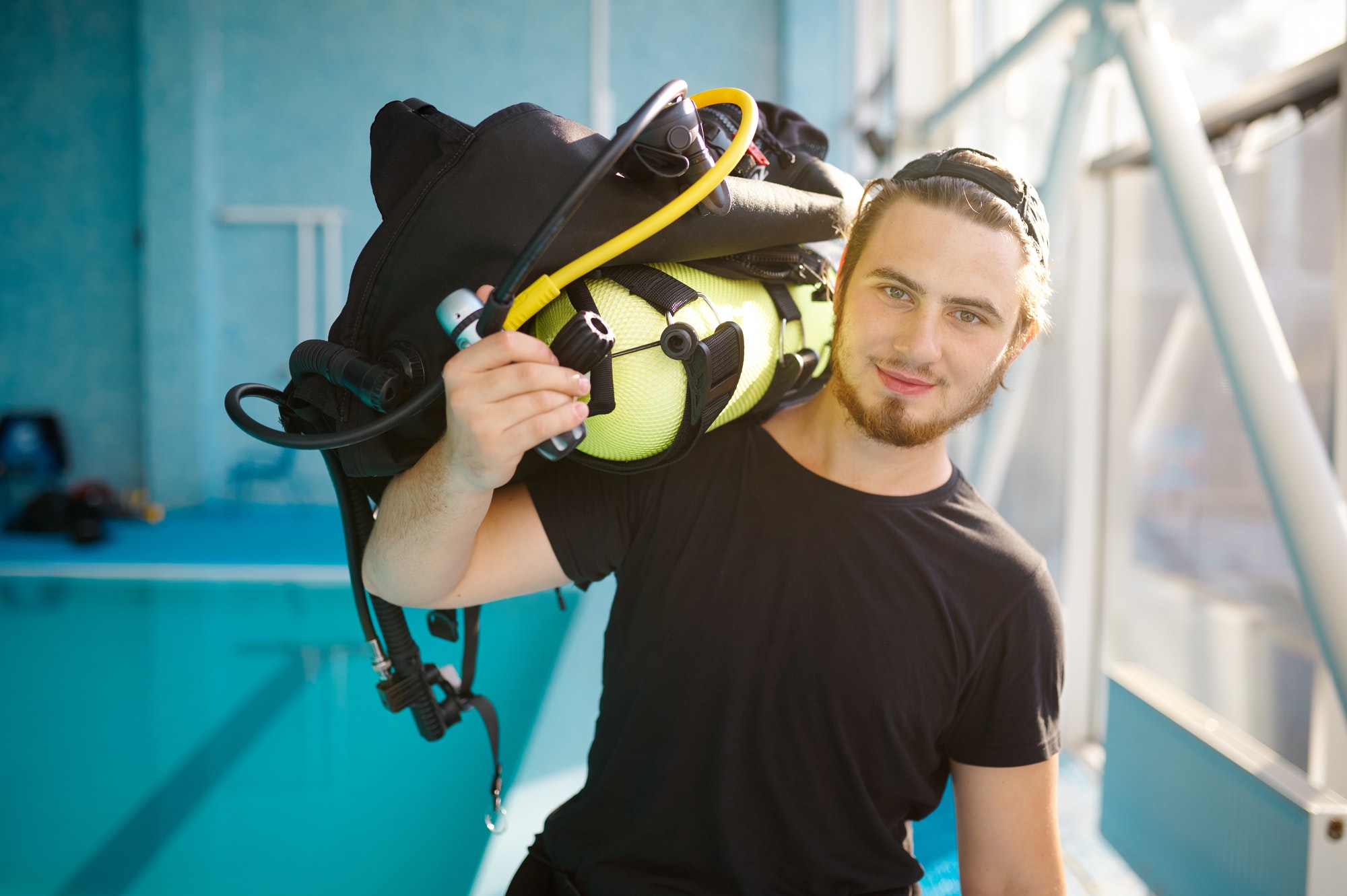 Male diver holds scuba gear, diving school